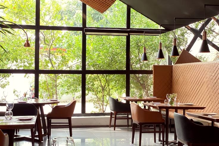 A dining room with a glass wall onto trees and dark timber chairs