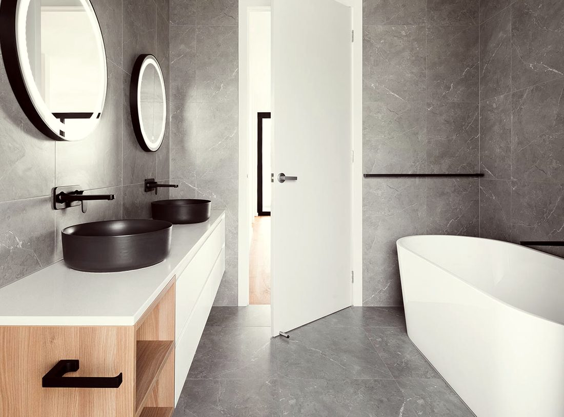 A grey stone bathroom with a freestanding tub and a round mirror