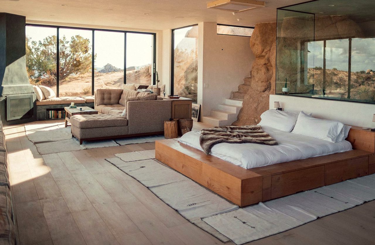 A suite with a stone wall, a timber bed and a window onto rock and scrub